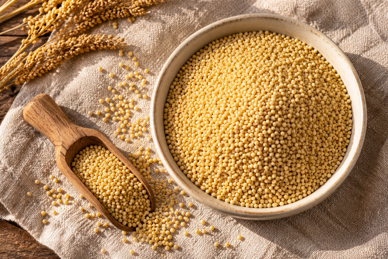Chinese millet cooking illustration with tiny hulled golden grains in a ceramic bowl beside a wooden scoop